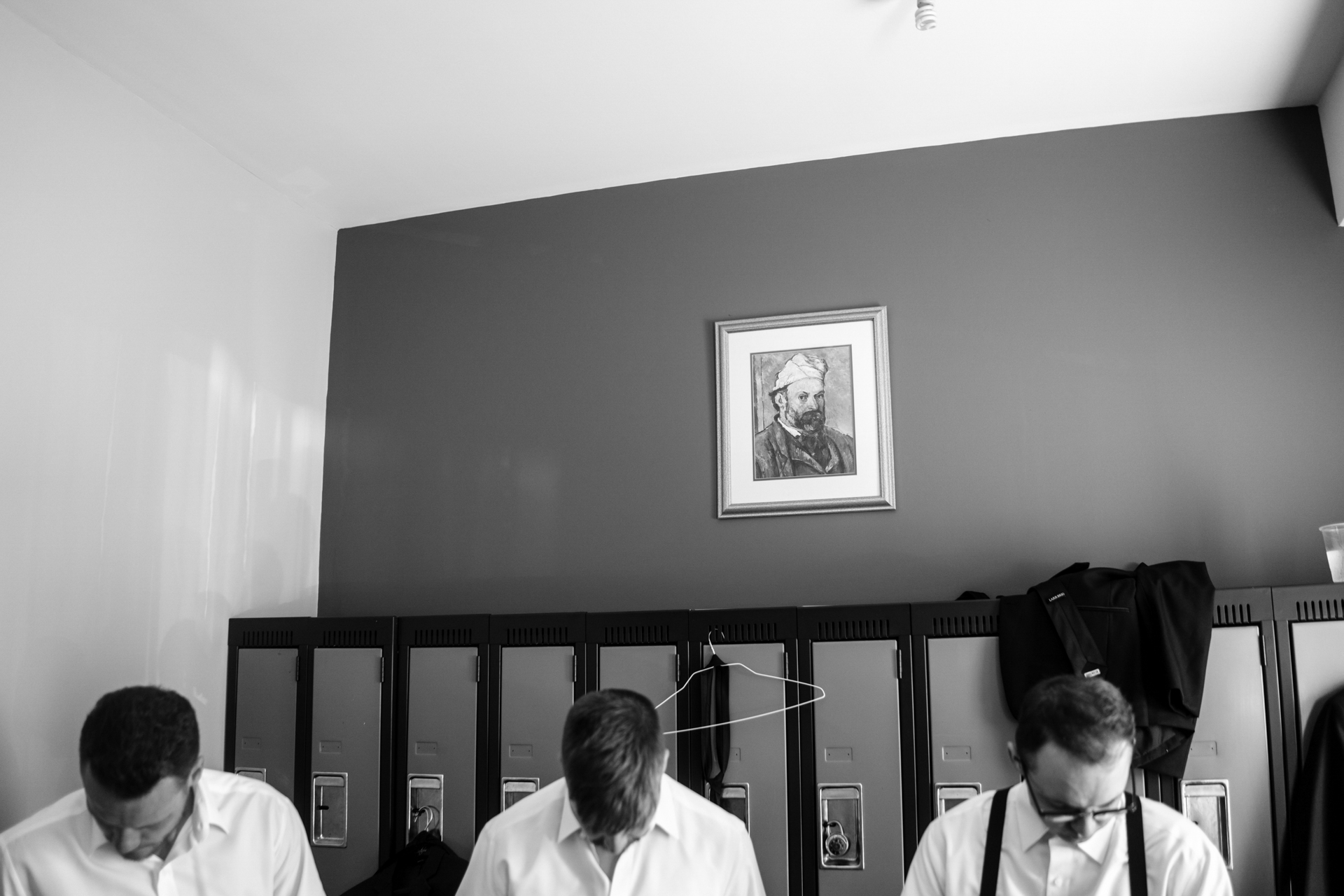 three groomsmen are taking clothes on in front of a portrait painting on the wall in the wedding day morning taken by documentary wedding photographer cafa liu